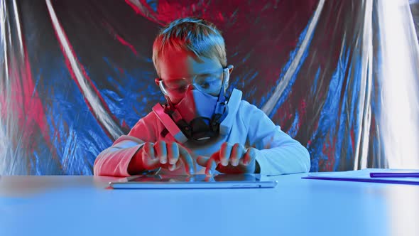 Young Boy Scientist Wearing Protective Hazmat Suit and Face Shield Using Tablet in a Laboratory