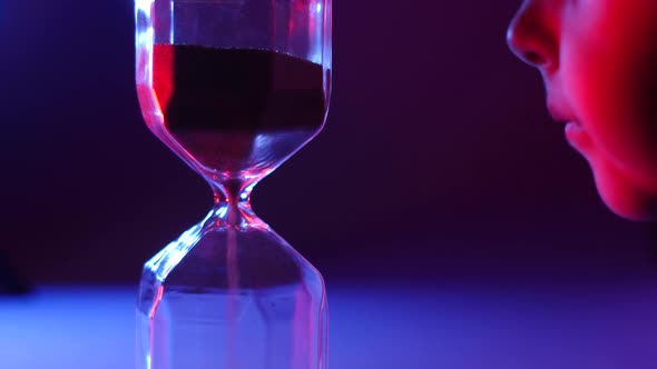 Boy Child Looks at Glass Hourglass in Blue and Red