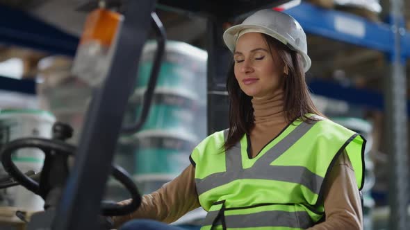 Charming Coquette Caucasian Woman in Hard Hat Sitting in Warehouse Autoloader Turning Looking at