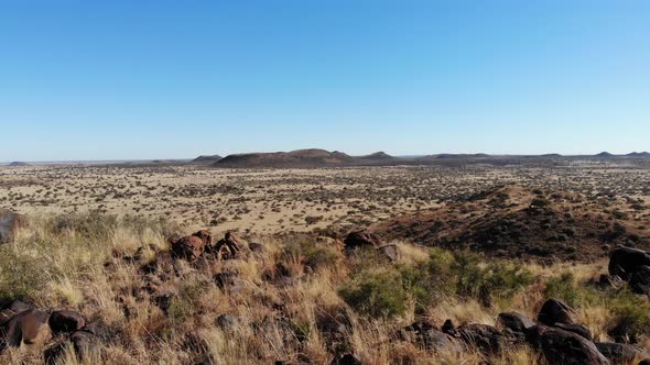 A wide shot moving from the top of a hill reveals a large African savanna under a bright blue sky.