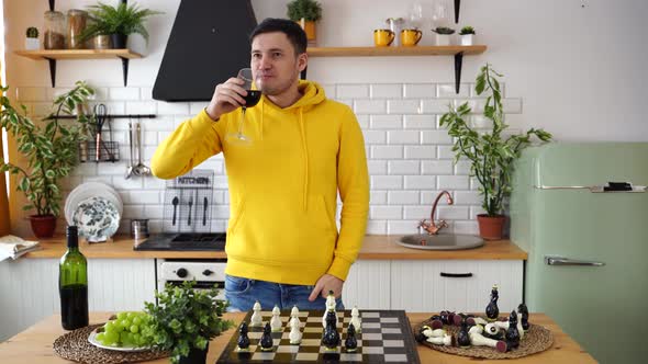 Young Man Playing Chess on Kitchen Table and Drinking Red Wine