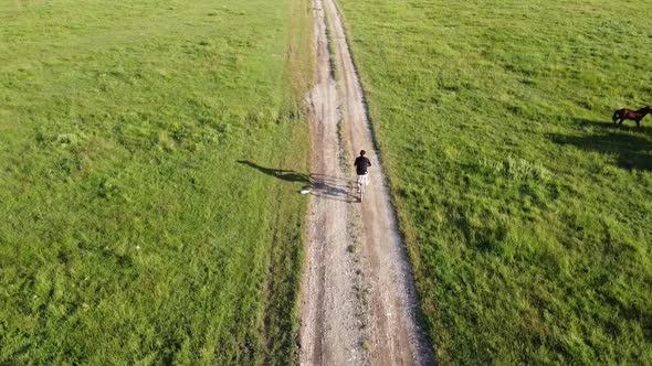 Aerial footage of a male ridding his bike on a country road on a sunny summer day