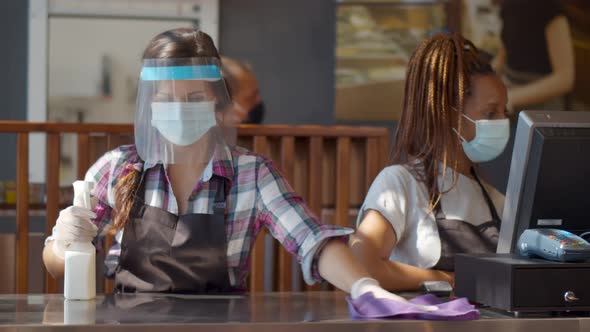 Waitress in Protective Face Mask and Shield Disinfect Counter Standing Near Cashier in Cafe