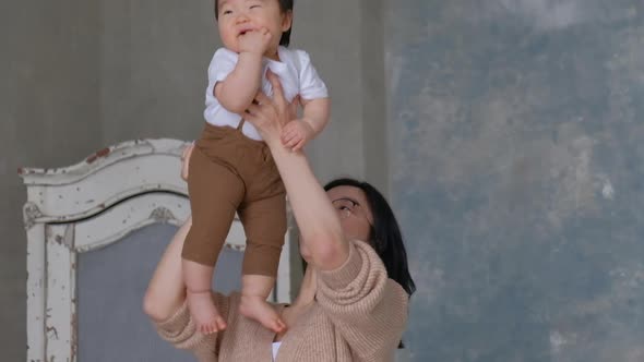 Happy Asian young mother throws her son up, smiles and laughs