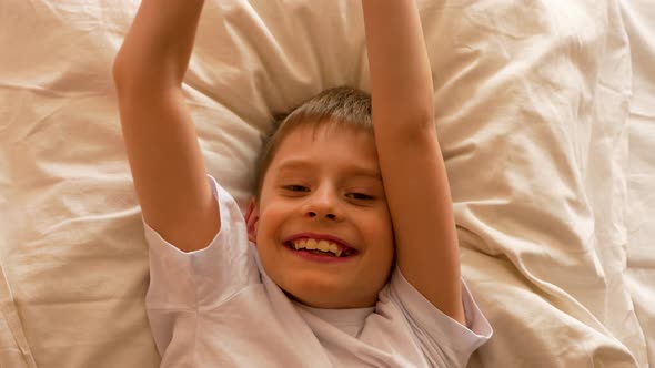 Morning awakening Caucasian boy 6-9 years old in bed. Positive boy wakes up in sunlight