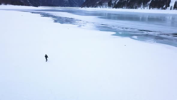 The drone orbits around a young east european guy with a camera who walks through a snowy field. In