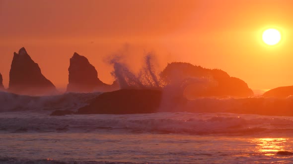 A slow-motion shot of a large wave crashing in red light with the sun orb setting behind it.