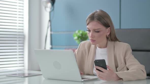 Businesswoman Using Smartphone While Using Laptop in Office