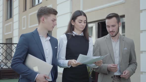 Young Woman and Two Men in Formal Wear Walking on Terrace Discussing Project