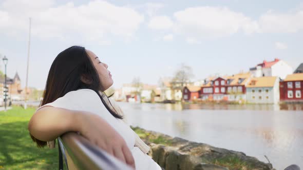 Asian woman sitting and  putting her hand on a chair by the river