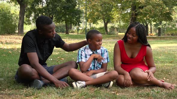 A Young Black Family Sits on Grass in a Park and Enjoys the Time Together