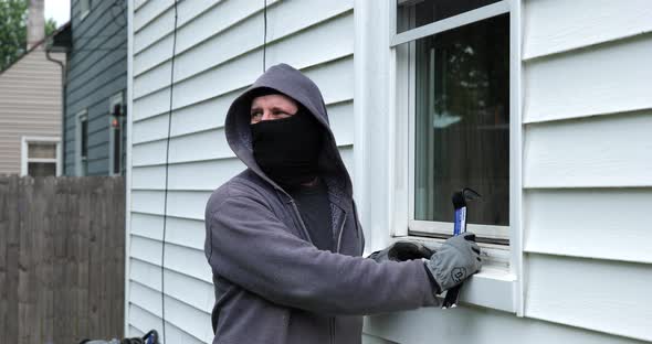 Burglar pries open a window with a crowbar and starts to climb into a home