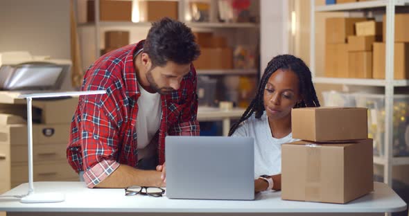 Diverse Young Man and Working on Laptop at Warehouse for Online Seller