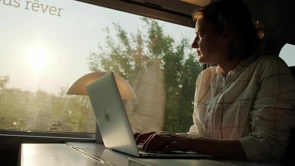 Woman Works on Laptop While Riding Train Sitting Near Window on Sunny Day