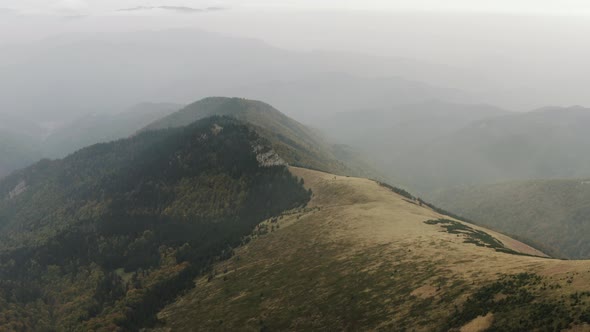 Ascending aerial shot of foggy peak covered with few evergreens, Slovakia