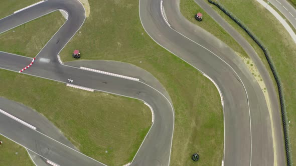 Aerial Top Down View Drone Flies Over White Racing Car Driving on Winding Race Track. Cloudy Summer