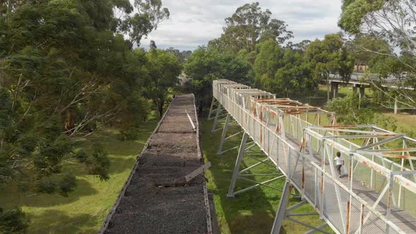 Forward moving aerial shot of little boy running on a metal bridge next to an old wooden rail way br