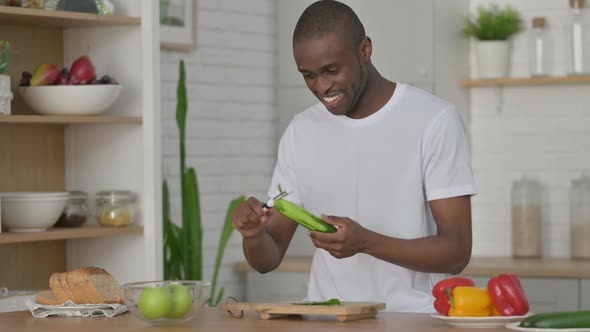 Healthy African Man Peeling Cucumber in Kitchen