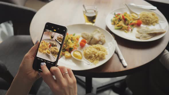 Woman Blogger Takes Pictures of Her Food in a Cafe Using Mobile Phone.