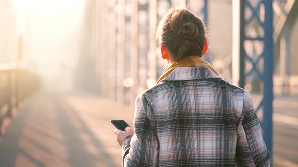 Portrait of a Young Caucasian Businesswoman in a Coat Walking Across the Bridge on a Frosty Morning