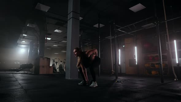 A Strong Woman Makes Efforts and Overcoming Difficulties Lifts a Dumbbell in a Dark Gym