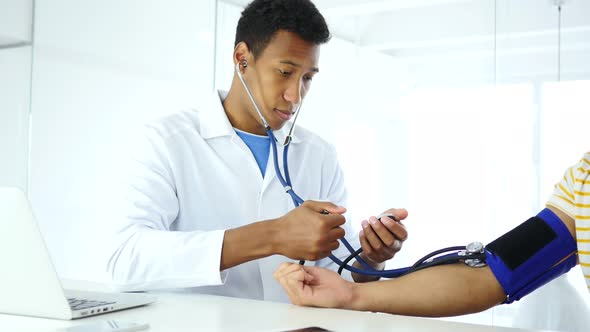 Afro-American Doctor Checking Blood Pressure of Patient in Clinic