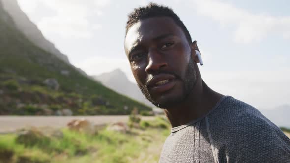 African american man listening to music putting earphones in while exercising in countryside