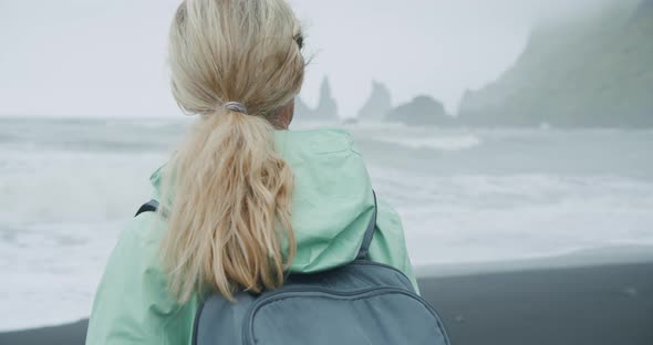 Woman with a Green Raincoat Walking on a Black Sand Beach Enjoying View to Reynisfjara Sea Stack