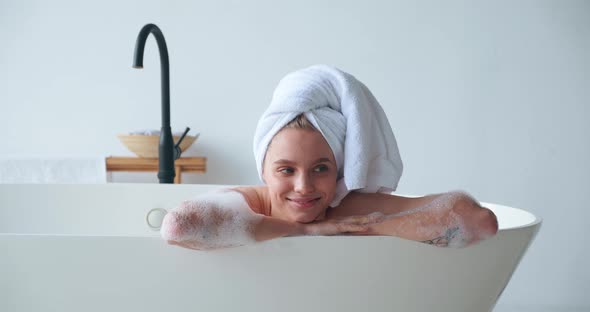 Charming White Woman with Closed Eyes of Pleasure Lying in Bathtub and Taking Bubble Bath Playing