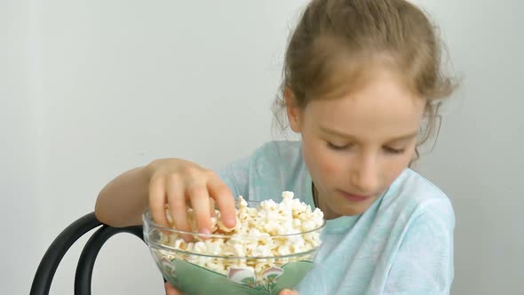 Portrait of a Funny and Excited Schoolgirl Girl on a White Background Smiling and Eating Popcorn