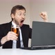 Happy businessman in suit sitting in front of laptop and holding glass of beer. - VideoHive Item for Sale
