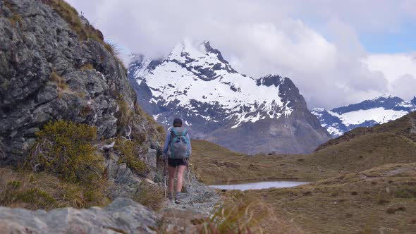 Slider, hiker walks alpine terrain towards distant snow capped mountains, Routeburn Track New Zealan