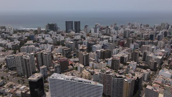 Drone shot of a coastal city on a sunny clear day and the Peruvian flag in Lima on the foreground