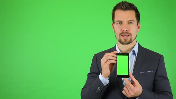 A Young Businessman Talks To the Camera and Holds Out a Smartphone with Green Screen