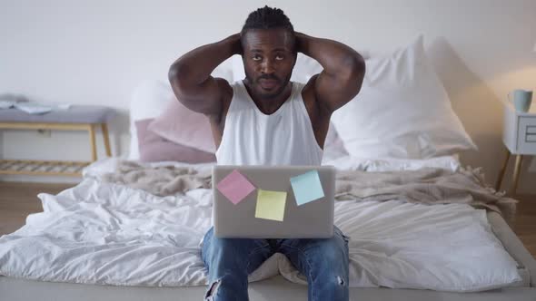 Front View of African American Young Man Leaning Back on Bed As Laptop Falling and Guy Catching