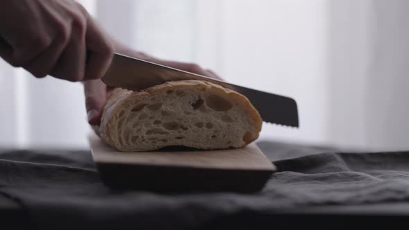 Slow Motion Man Slicing Ciabatta on Olive Board with Window on Backgorund