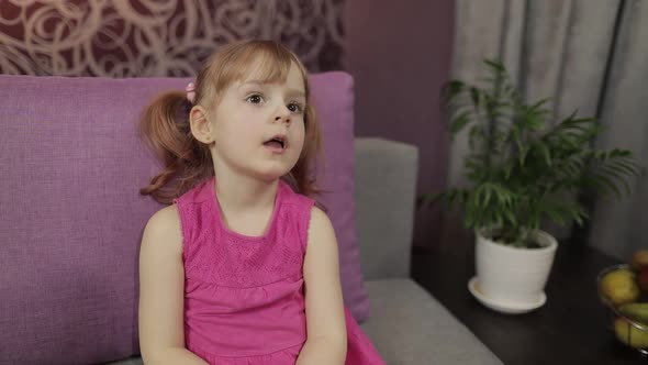 Little Child Sitting on Couch While Watching TV. Kid Girl Watch Television