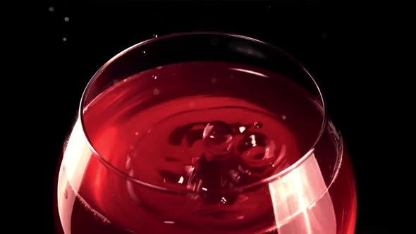 Super Slow Motion Drop with Splashes Falls Into a Glass of Wine