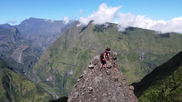 Drone footage of two people climing steep rock in front a scenery of the Cirque of Mafate at the Reu