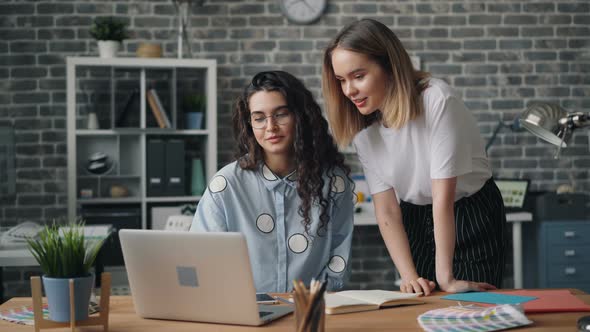 Young Girls Colleagues Talking and Laughing Looking at Laptop Screen in Office