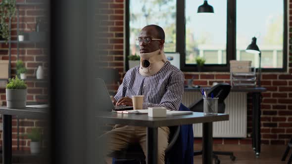 Businessman with Medical Neck Collar Working on Laptop