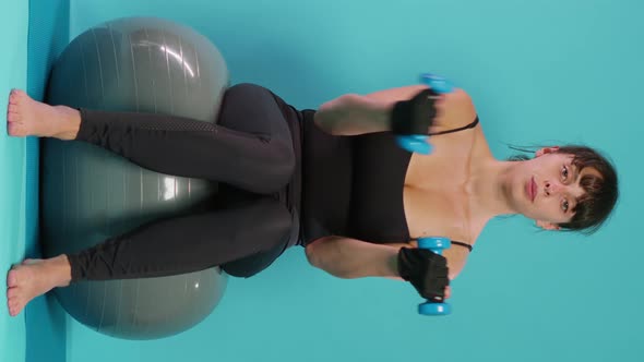 Vertical Video Fit Person Using Dumbbells to Lift Weights on Fitness Toning Ball