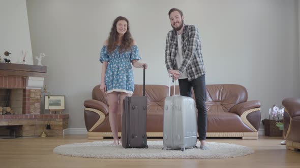 Portrait of Happy Smilling Couple Standing with Big Suitcases at Home. Young Bearded Man and Young