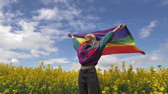 Female with LGBT rainbow flag on yellow rapeseed field in spring