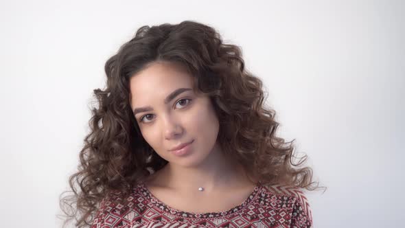 A young woman with long curly hair with a calm expression looks at the camera