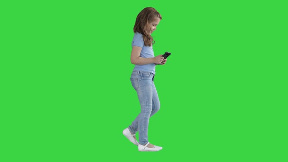 Little Girl Is Playing with Smartphone While Walking on a Green Screen, Chroma Key