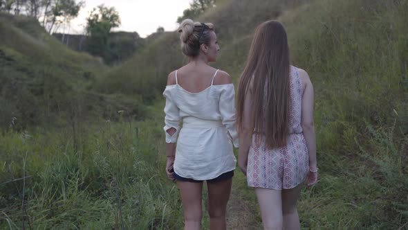 Back View of Confident Caucasian Mother Strolling with Adult Daughter Outdoors on Overcast Day