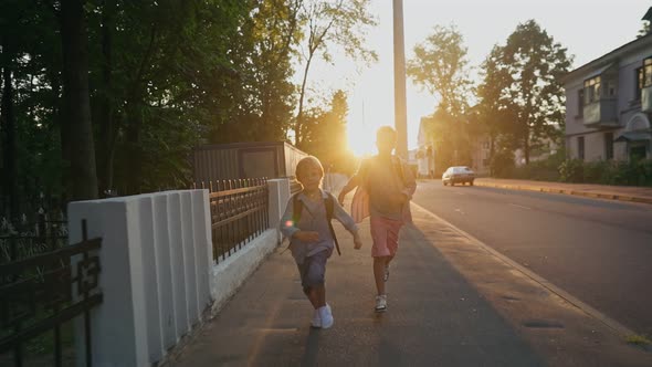 Two Schoolboys with a Backpacks Running on Street at Sunset Time