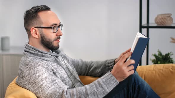 Handsome Bearded Guy in Glasses Reading Paper Text Book Lying on Couch