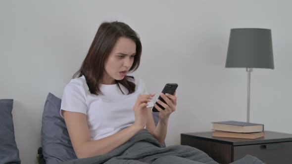 Woman Reacting to Loss on Smartphone in Bed